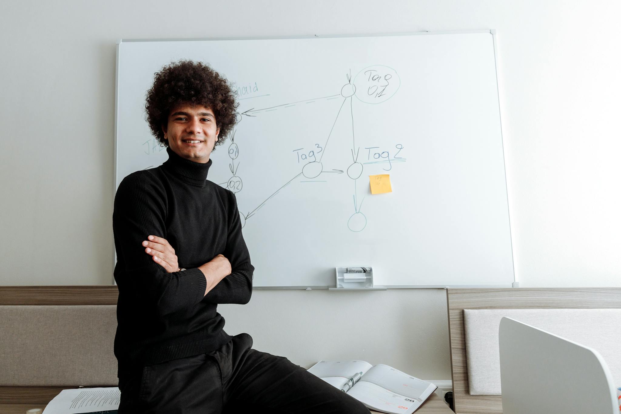 Young professional sitting in office smiling confidently by a whiteboard.